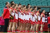 Sydney Swans AFL players and their head coach stand side by side as they acknowledge a minute's silence.