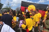 A number of Indigenous protesters wear yellow shirts and hold a large Aboriginal flag.