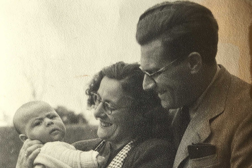 A black and white photo of parents holding and looking at a baby.