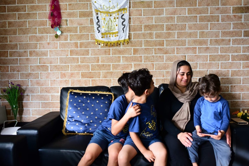 A woman hugs three children on a sofa.