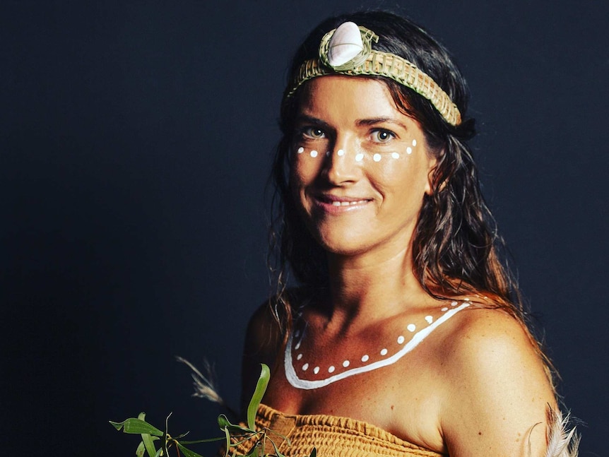 Young Aboriginal woman with white ochre dot painting under her eyes and over collarbone wearing woven grass headband with shell