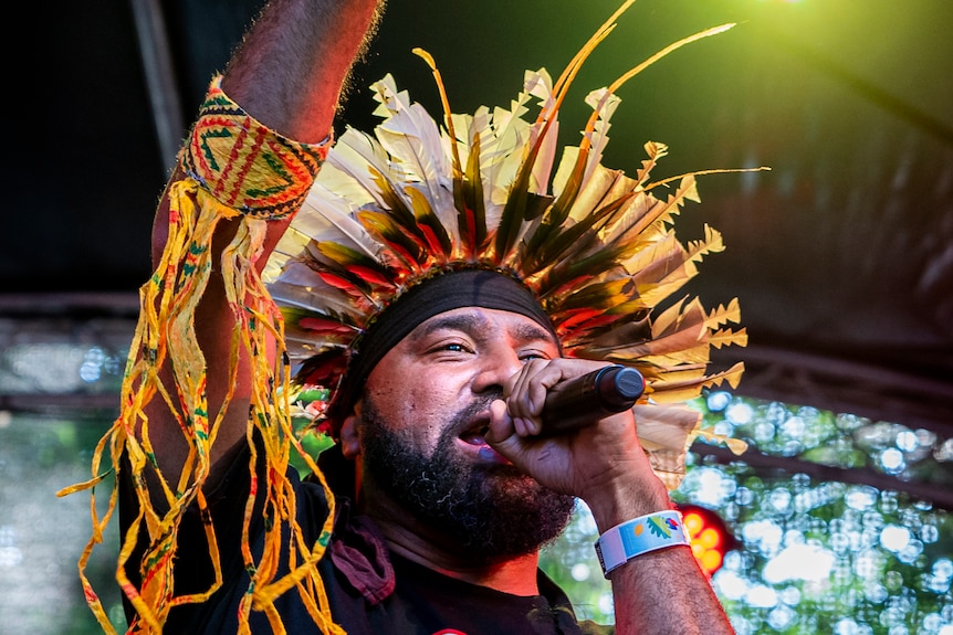 A man singing on stage in tribal headwear.