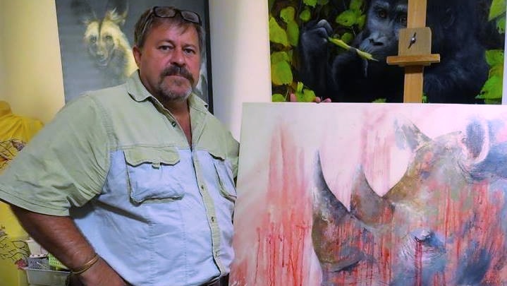 Rhino conservationist Marc McDonald stands in front of a painting of a rhino, splashed with red paint resembling blood