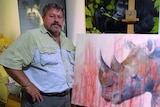 Rhino conservationist Marc McDonald stands in front of a painting of a rhino, splashed with red paint resembling blood