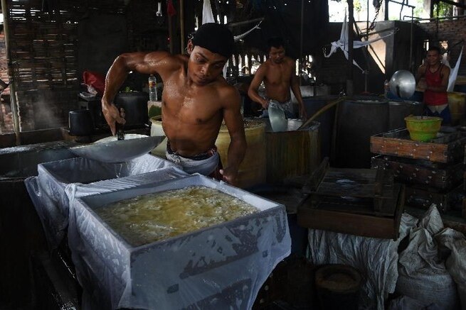 A shirtless man making tofu in a steaming tofu factory.