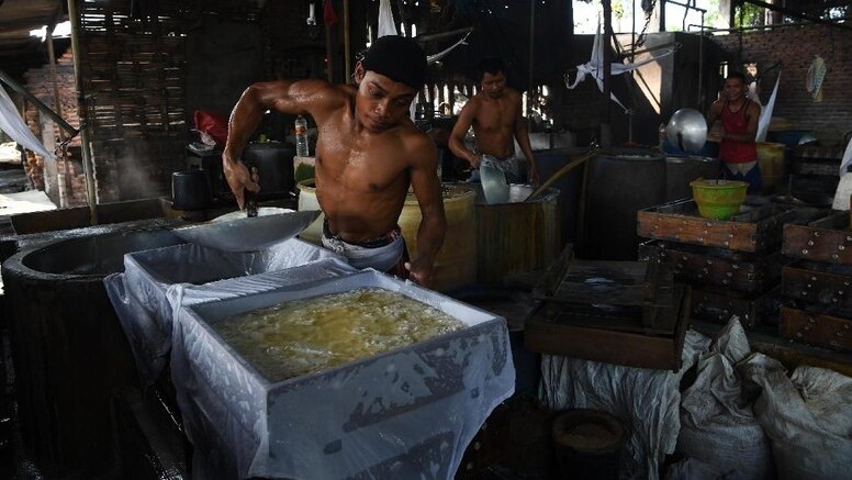 A shirtless man making tofu in a steaming tofu factory.