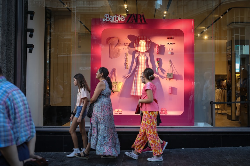Women walk past a shop front made to look like a flat lay of Barbie's pink clothes and accessories.