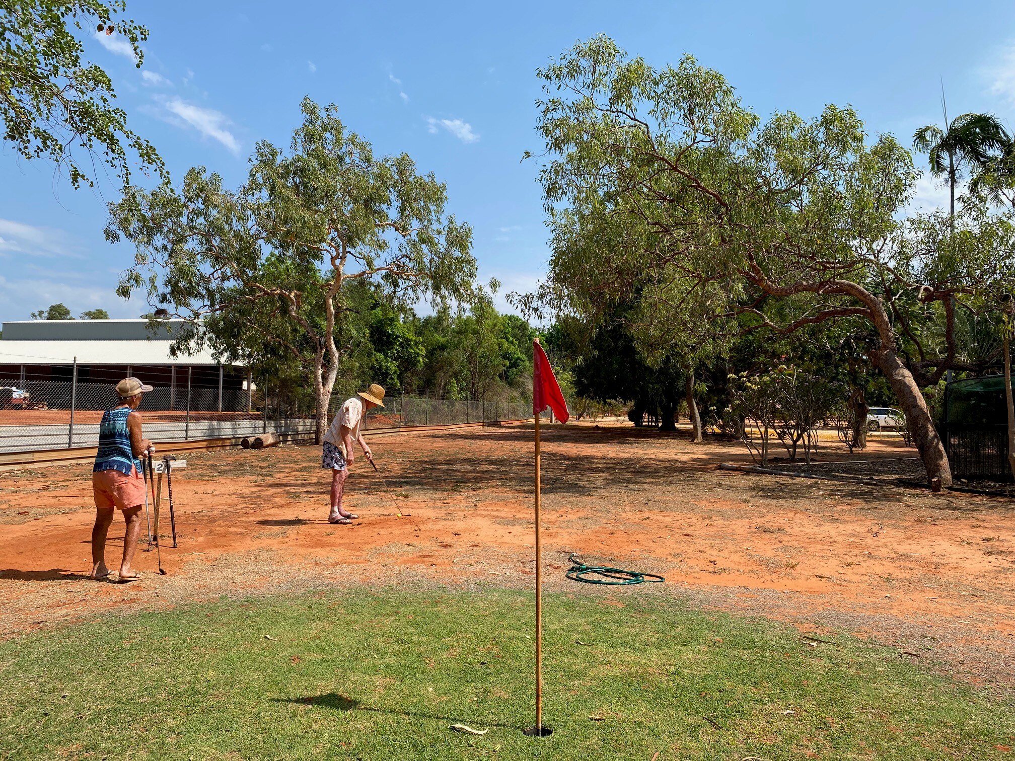 Red fairways beyond a green lawn with a flag, while golfers hit
