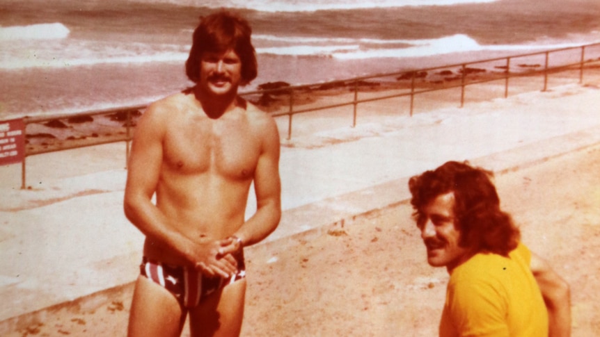 A shirtless Ken Holloway stands on a Jersey beach with a friend.