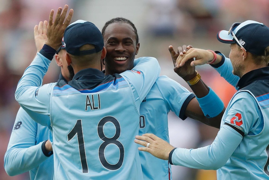 Jofra Archer smiles as he is hugged by his England teammates wearing light blue cricket kit