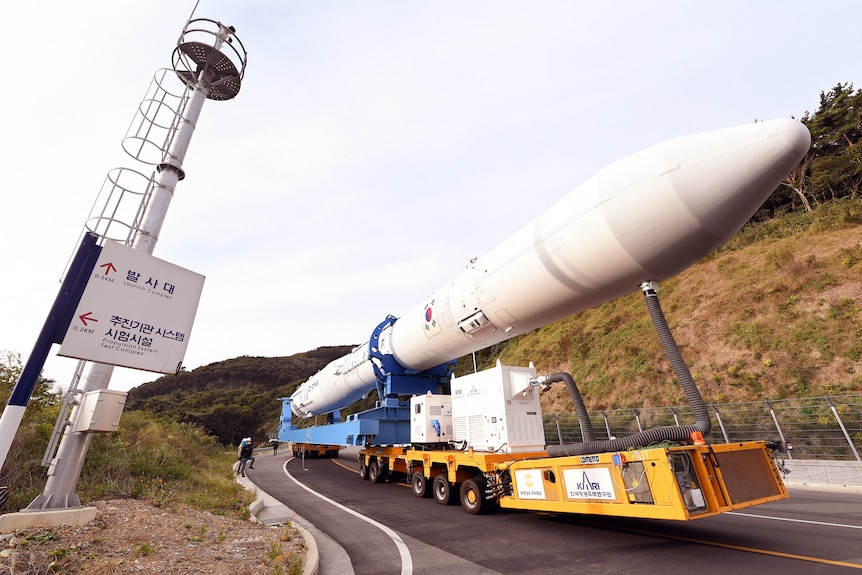 A white rocket is carried on wheels on a hilly road 