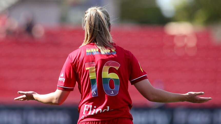 A soccer player wearing a red jersey with rainbow numbers