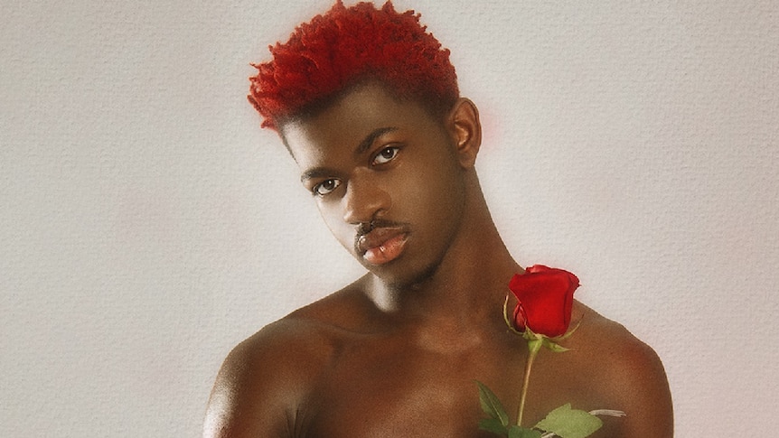 Image of African American male with red dyed hair, shirtless, holding a rose