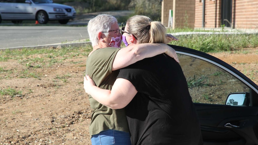 two ladies wearing masks hug next to car