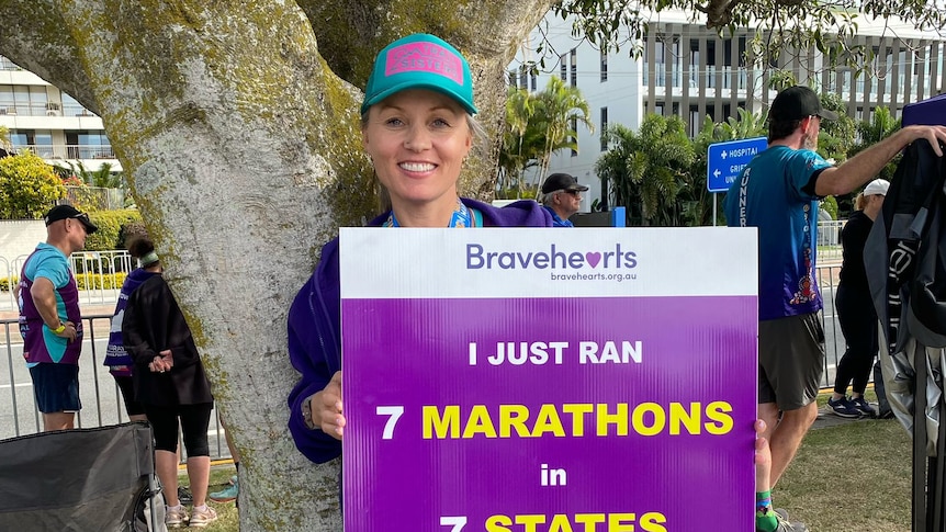 Athletic woman smiling at camera holding a sign which says I ran 7 marathons in 7 days in 7 states