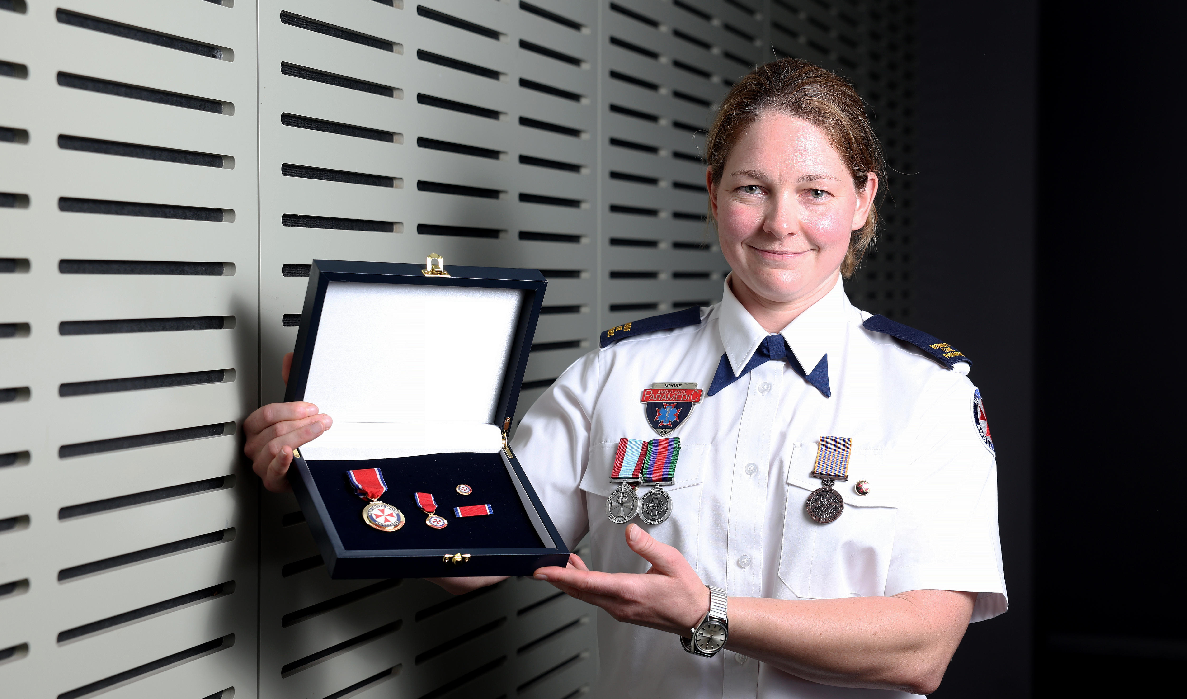 Harriet holds her medals box and smiles, wearing her formal uniform.