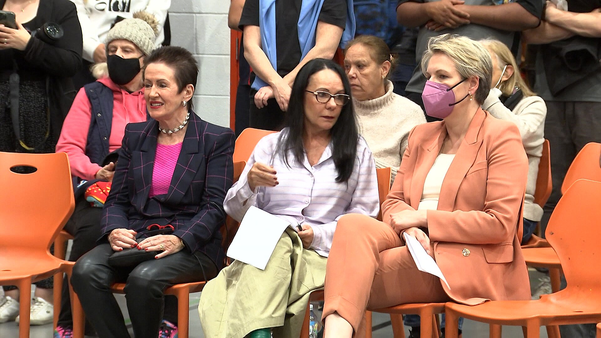 three women sitting on chairs at a public meeting