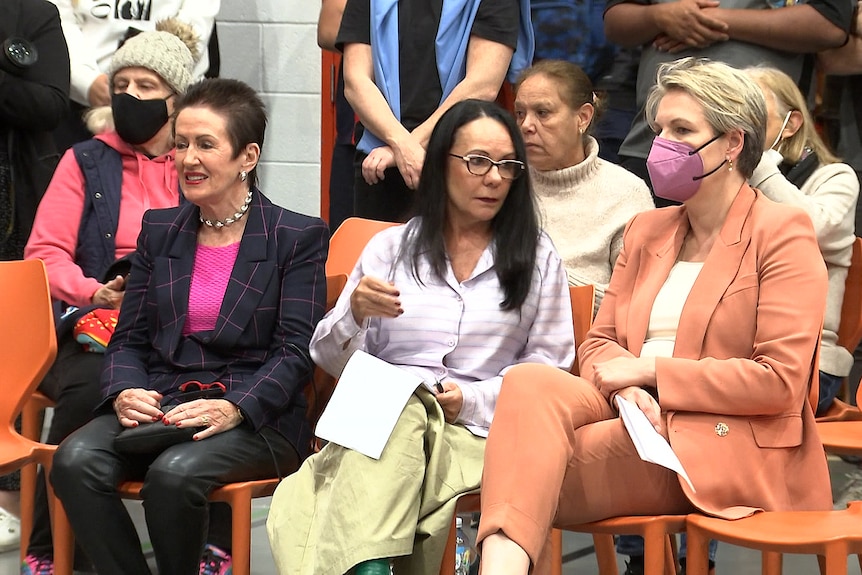 three women sitting on chairs at a public meeting