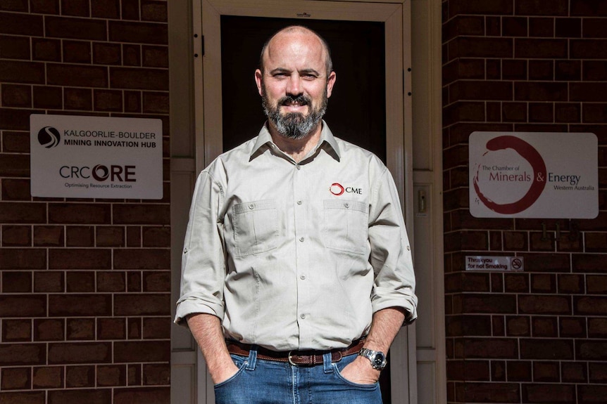 Man stands in shirts and jeans on verandah with hands in pockets