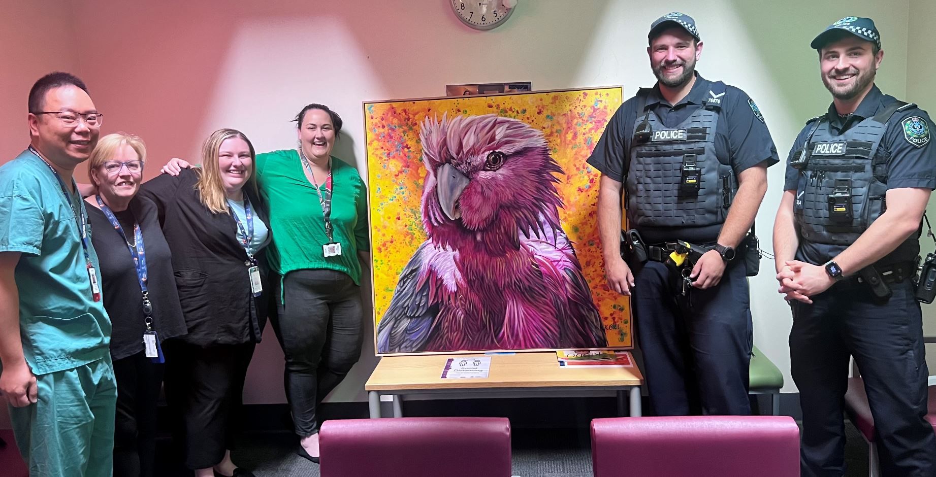 A group of medical staff and police smiling next to a galah painting.