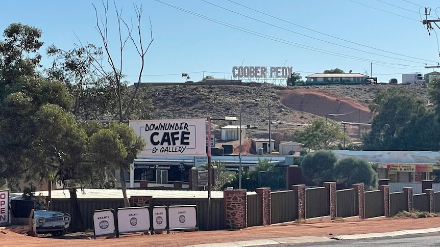 A hill with Cooper Pady sign, beneath it Downunder Cafe and gallery, blue sky, trees in front of cafe.