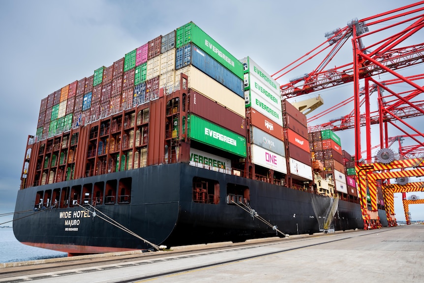 A cargo ship full with shipping containers docked at a Sydney port.