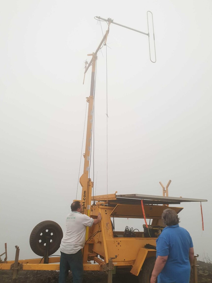 Two people operating a yellow machine with a radio signal at the top.