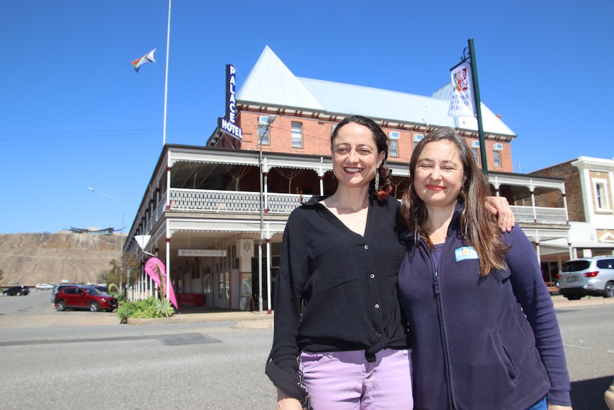 Two women standing together outside the Palace building smile, one with a black cardigan another with a jacket