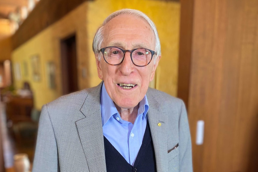 An elderly man wearing a suit jacket, vest and open-necked collar.