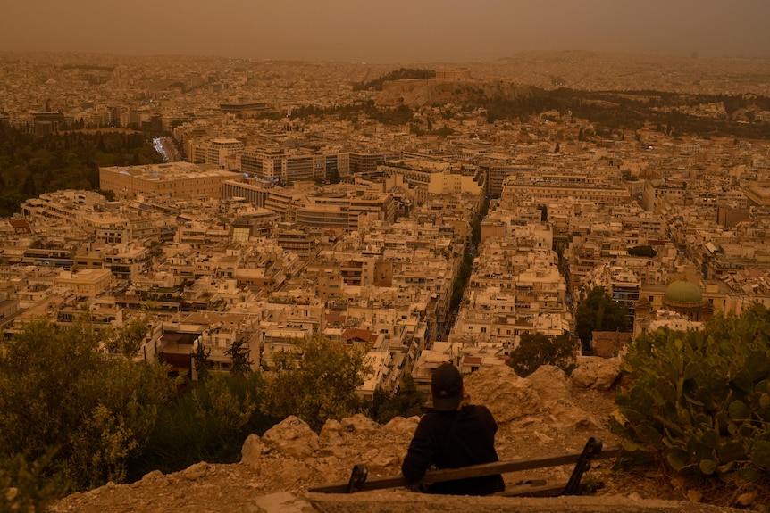 Tourist looks out at orange haze over city of Athens.