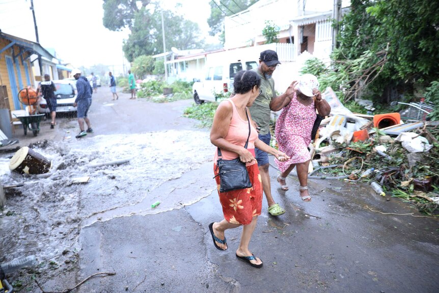People run through the rain down a suburban street as water flows over the road behind them.