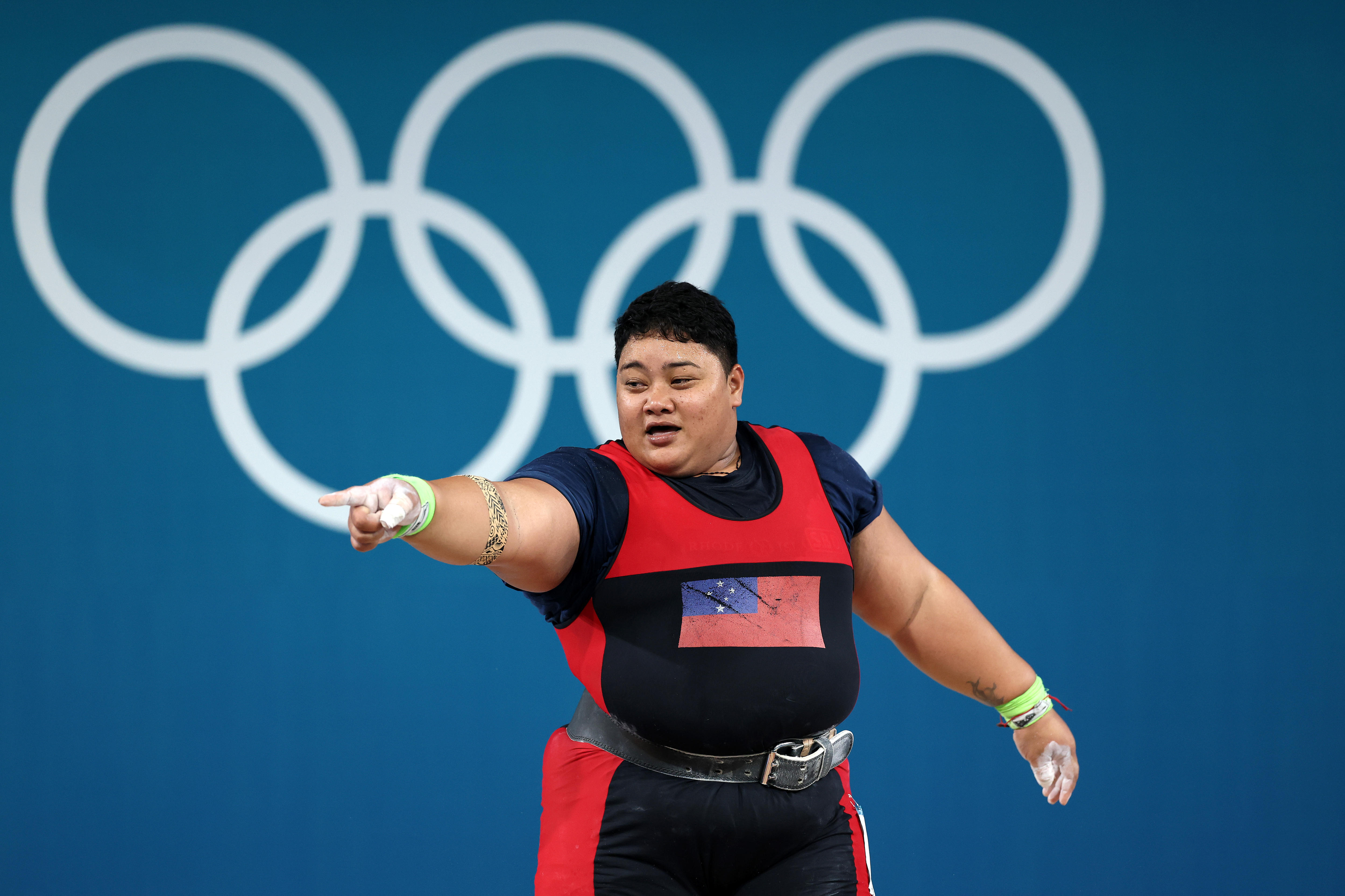 Uma mulher samoana aponta para a multidão vestida com equipamento de levantamento de peso.