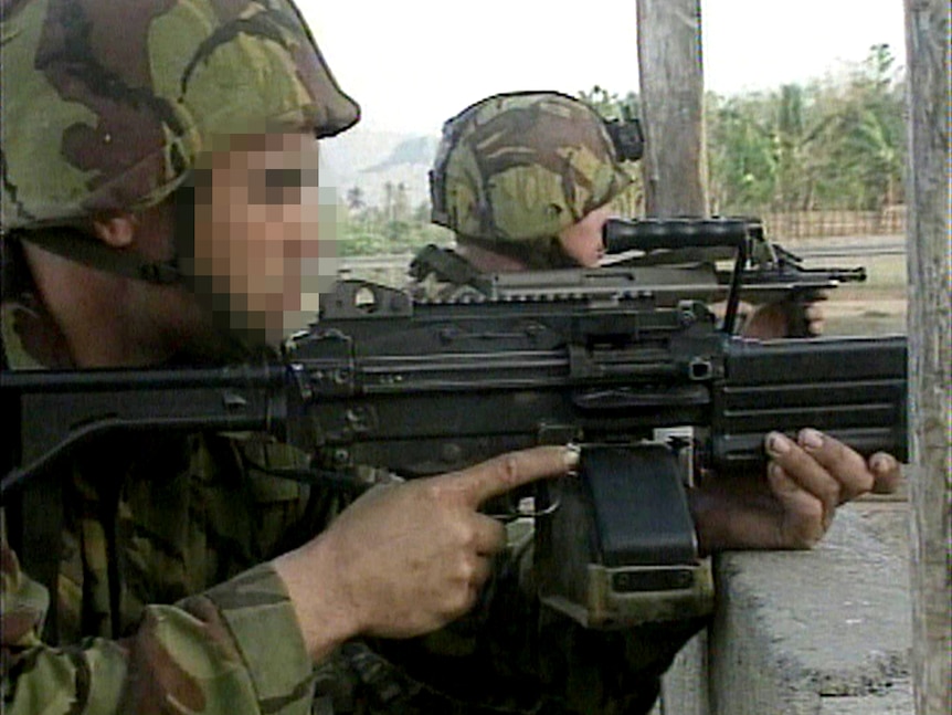 Two soldiers in camouflage are seen from the side firing their weapons.