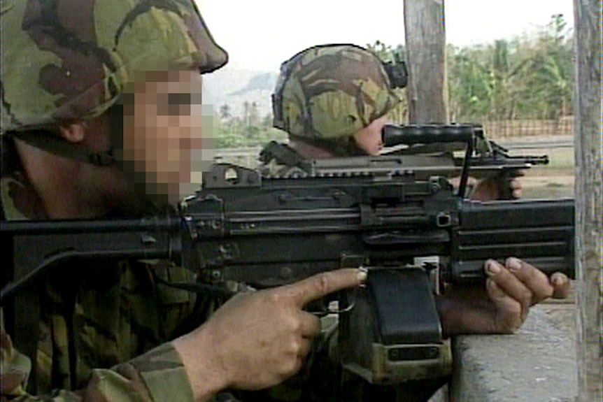 Two soldiers in camouflage are seen from the side firing their weapons.