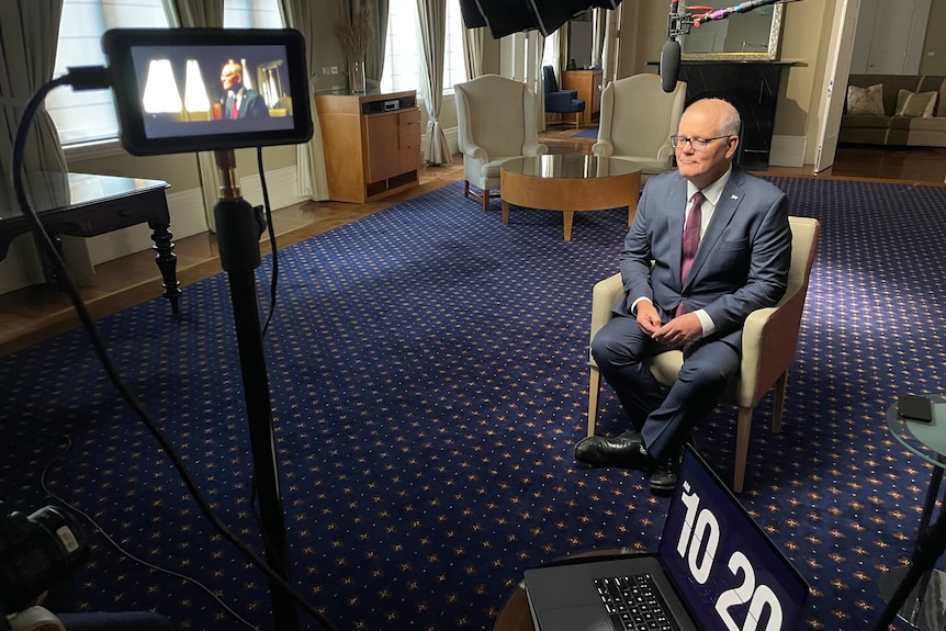 A wide shot showing Scott Morrison in a chair being interviewed, surrounded by camera and lighting equipment.