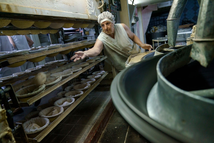 A woman tossing a ball of dough into a basket on a shelve with several baskets on it