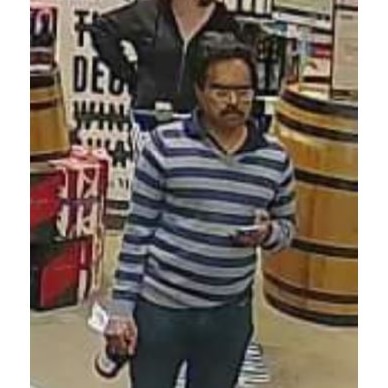 A man in a striped top holding a bottle walks through a bottle shop.