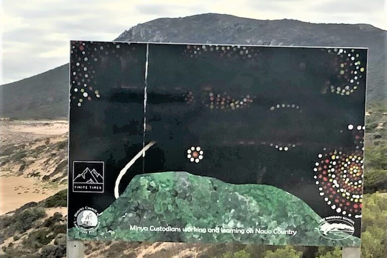 A sign with black paint over it, on clifftop above beach