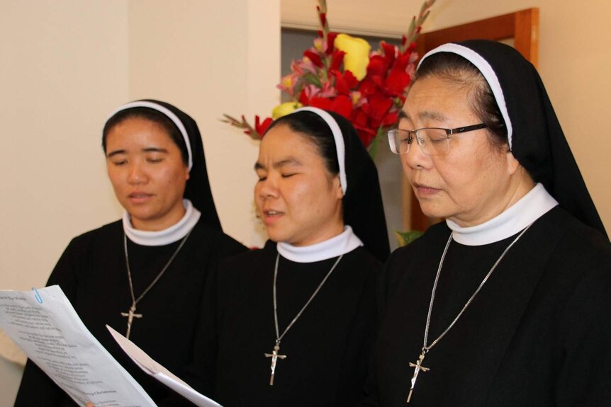 Three nuns read from pieces of paper in a church