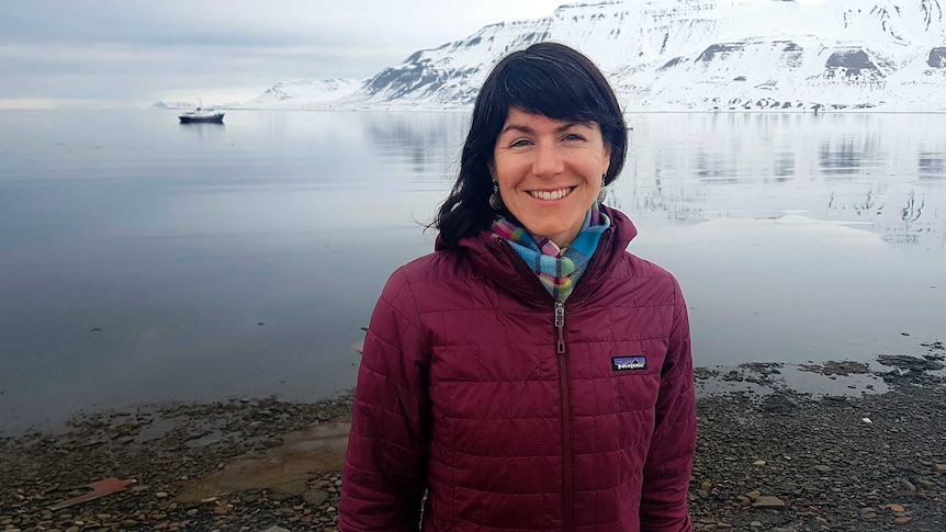 Sarahj Auffret has dark long hair and is smiling against a backdrop of an snowy archipelago in Svalbard.