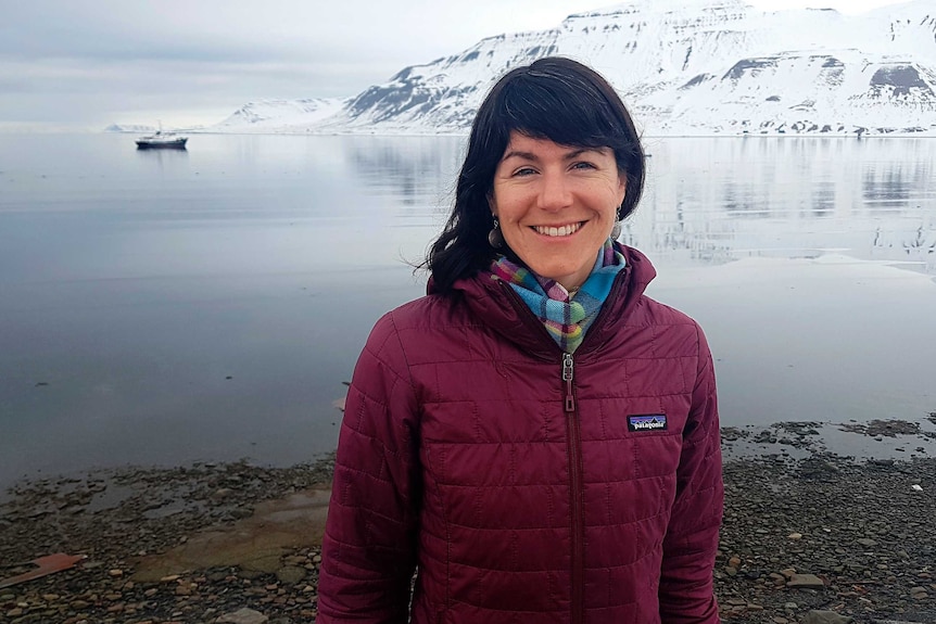 Sarahj Auffret has dark long hair and is smiling against a backdrop of an snowy archipelago in Svalbard.