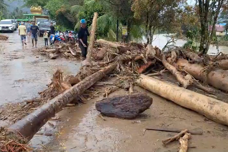 A man attempts to clear logs and debris from a flooded road