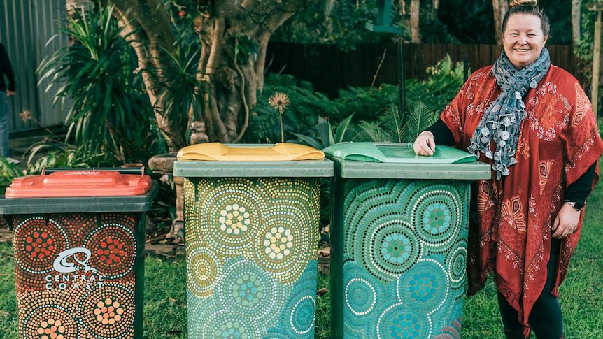 Ang Bennett stands with painted rubbish bins with her arm on top