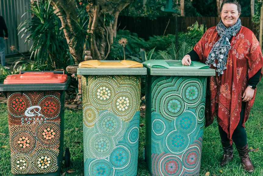 Ang Bennett stands with painted rubbish bins with her arm on top