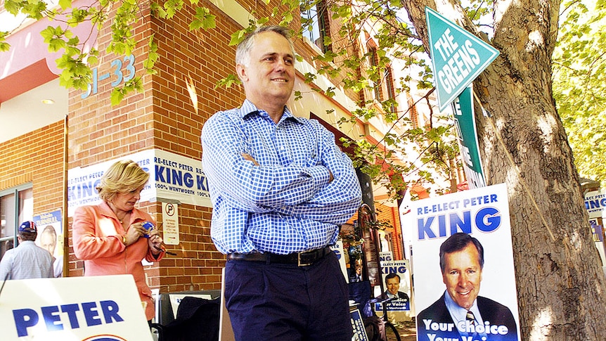 Former Prime Minister Malcolm Turnbull standing with his arms crossed surrounded by posters saying "Re-elect Peter King"