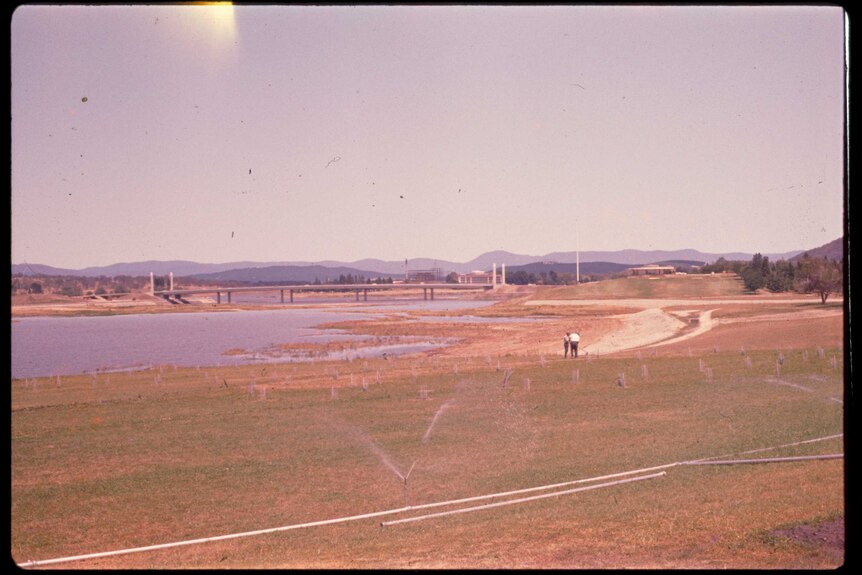 An old photo shows Lake Burley Griffin still filling, looking towards Commonwealth Avenue Bridge and Regatta Point.