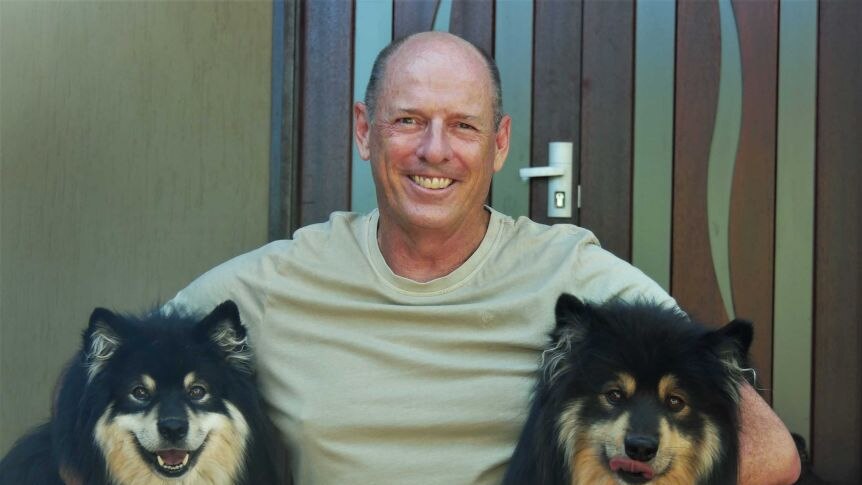A man cuddles two fluffy black and tan dogs