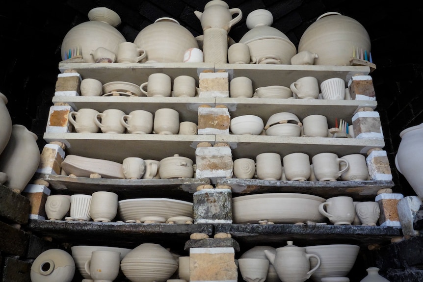 Unfired ceramic pots, cups, bowls and plates packed tightly into shelves of kiln.