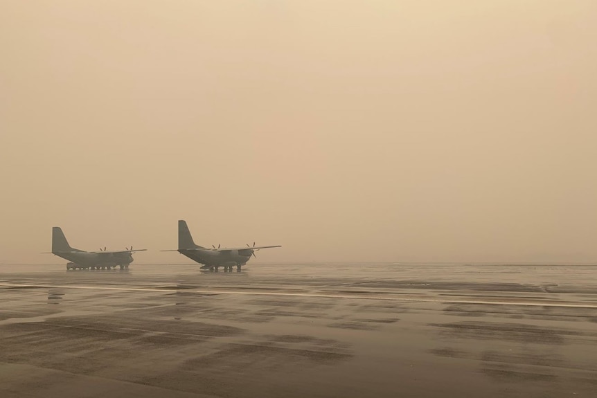 Two army planes on the tarmac in a thick smoke haze.