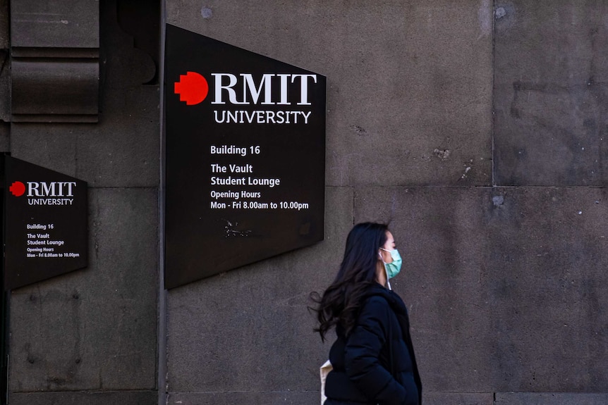 Woman in face mask walking past RMIT University sign